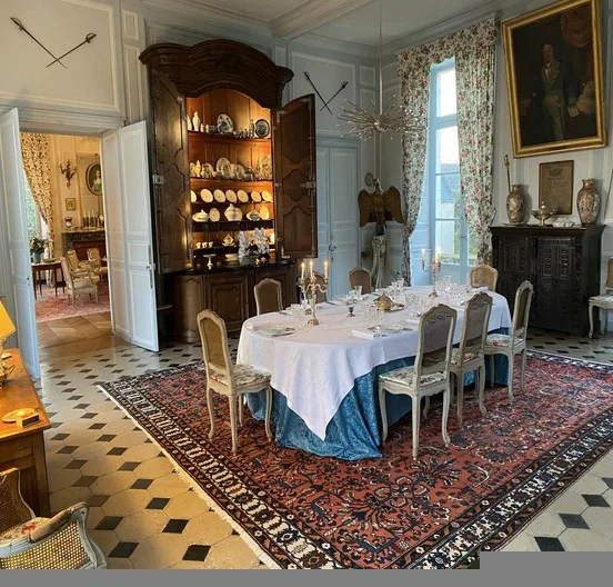 Grande salle à manger : table dressée, candélabres, portrait d'ancêtre et tapis persan sur carrelage