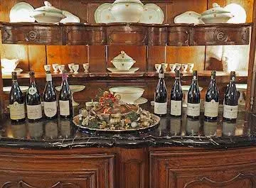 Bottles of red wine lined up on a sideboard around a festive centrepiece, porcelain tureens above