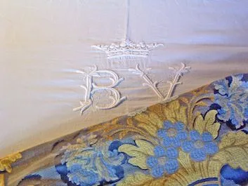 Crowned BV monogram embroidered in white on linen, over a blue and gold brocade bedspread