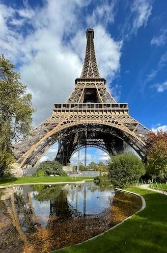 The Eiffel Tower in Paris reflected in a garden pond under a blue sky, autumn trees around it