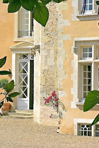 Château entrance in summer: pedimented glazed door, stone quoins and pink roses on the gravel