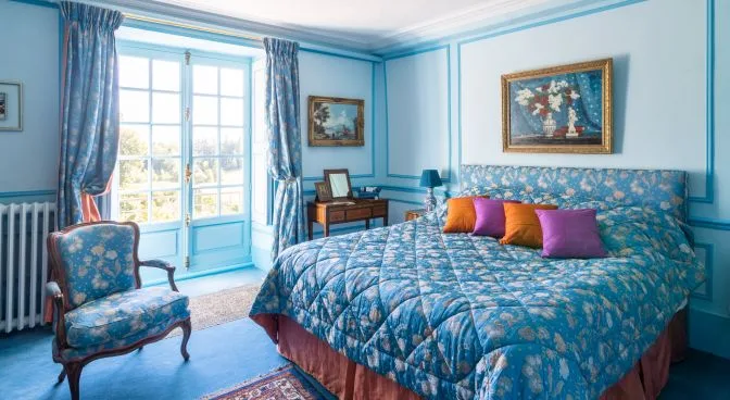 Chambre Turquoise: blue panelled walls, quilted bed, armchair and writing table by the French window